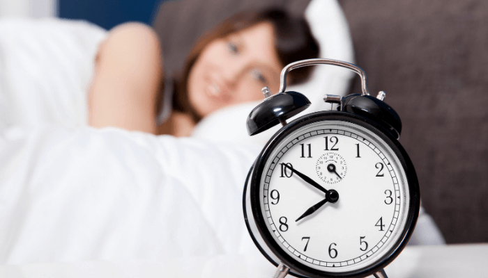 Black colored small alarm clock & a women smiling in the background