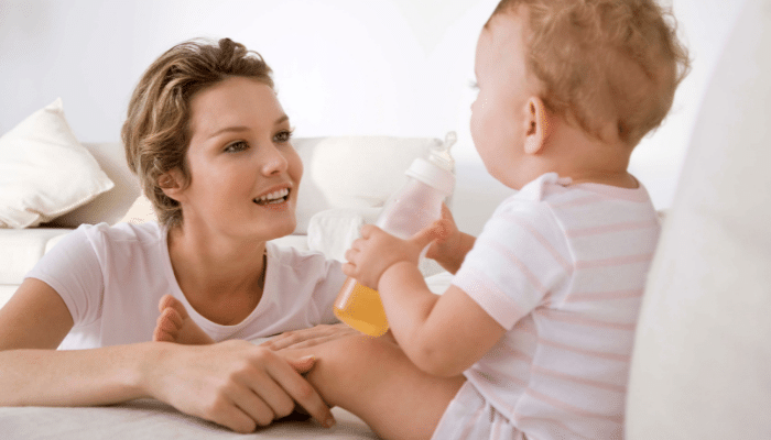 mom looking at baby sitting with bottle