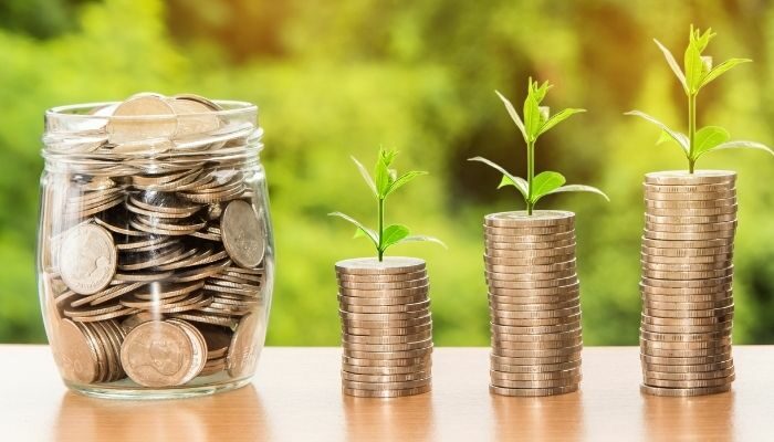 jar filled with coins and stacks of coin with leaves on top