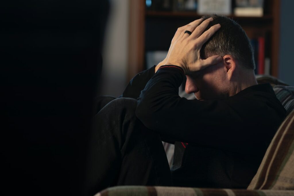 a man sitting on a couch holding his head in his hands
is 9 hours of sleep too much?