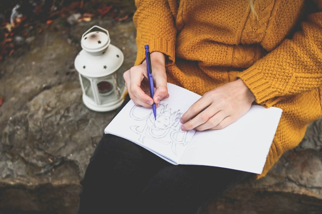 person drawing on sketch book near white lantern
